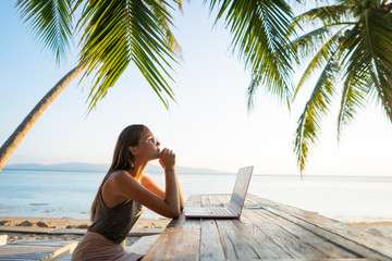 freelancer girl with a computer among tropical palm trees work on the island in sunset