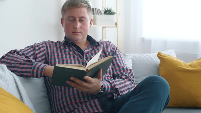 Man seat on sofa in living room and read interesting book. Relaxing after work. 4k. Slow motion.