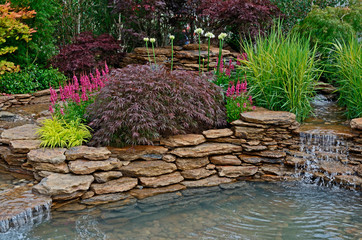 The pond area in an aquatic garden and planted rockery and selection of flowers, shrubs and grasses
