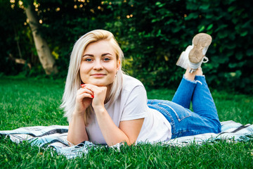 Beautiful blonde girl lying on plaid looking and smiling in frame on green grass background