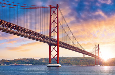 25th April Bridge in Lisbon, Portugal. Famous landmark on river Tagus. Summer sunny landscape with evening dusk sunset sky with clouds and sunlight.