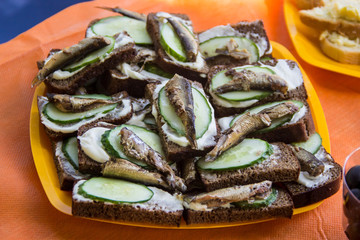 Sandwiches with smoked sprats and fresh cucumbers on an orange background