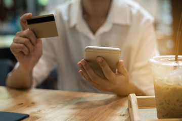 One woman hand hold mobile phone. On the other side, hold the credit card, To make shopping online in the coffee shop. On the table are iced coffee a business trip.