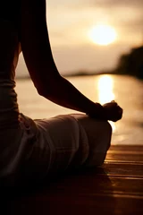  Rear view of Caucasian woman sitting in lotus position and meditating on dock at sunset. © chika_milan