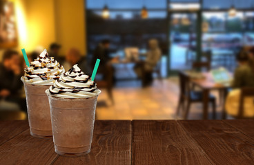 Iced coffee or frappuccino in plastic takeaway or to go cup on wooden table at cafe and people