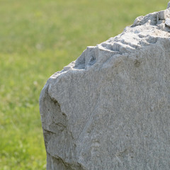 Detail of  a big grey stone from the side and a green field in the background.