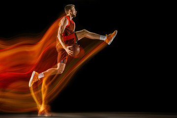 The fire tracks. Young caucasian basketball player of red team in action and jump in mixed light over dark studio background. Concept of sport, movement, energy and dynamic, healthy lifestyle.