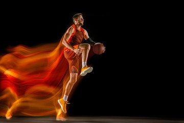 The fire tracks. Young caucasian basketball player of red team in action and jump in mixed light...