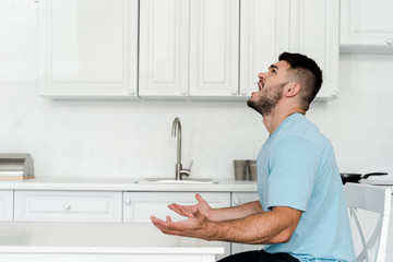 side view of upset man screaming while sitting near table in kitchen