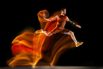 The fire tracks. Young caucasian basketball player of red team in action and jump in mixed light...