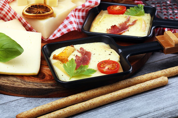 Delicious traditional Swiss melted raclette cheese on diced boiled or baked potato and baguette served in individual skillets with salami..