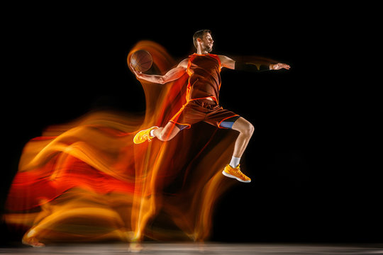 The fire tracks. Young caucasian basketball player of red team in action and jump in mixed light over dark studio background. Concept of sport, movement, energy and dynamic, healthy lifestyle.