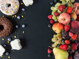 A lot of natural and healthy vitamin fruits, berries vs sweet and junk food on a black background. Vegan eco safe food. The right foods for weight loss and the wrong foods for weight gain. The choice