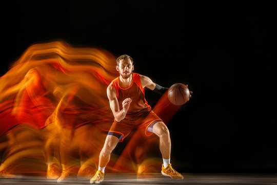 Becoming a winner. Young caucasian basketball player of red team in action and jump in mixed light over dark studio background. Concept of sport, movement, energy and dynamic, healthy lifestyle. © master1305