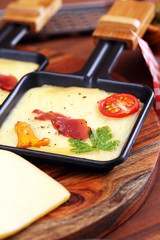 Delicious traditional Swiss melted raclette cheese on diced boiled or baked potato and baguette served in individual skillets with salami..