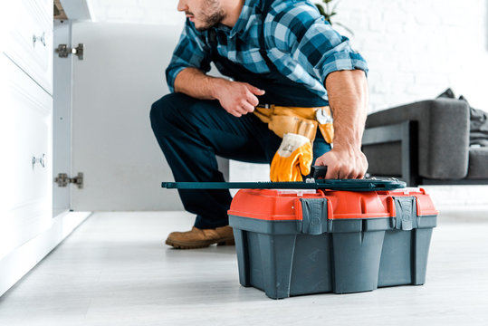 cropped view of bearded handyman sitting and holding toolbox