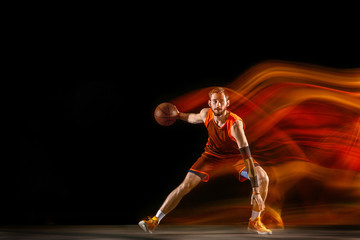 The comet. Young caucasian basketball player of red team in action and motion in mixed light over dark studio background. Concept of sport, movement, energy and dynamic, healthy lifestyle.