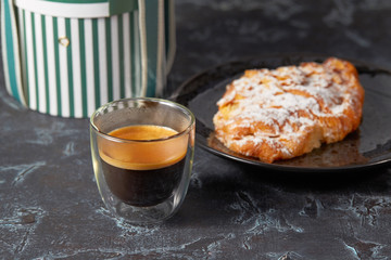 Cup of espresso with foam and an almond croissant on a plate on the background of a festive gift box with ribbons. Horizontal.