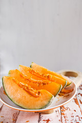 Fresh of sliced orange melon or cantaloupe on wooden cutting board on rustic white wood background.