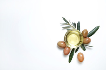 Bunch of local produce Turkish green gemlik olives with glass cup of extra virgin golden oil and olea europaea tree leaves. Close up, top view, copy space, isolated white background.