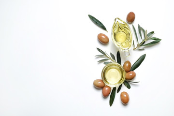 Bunch of local produce Turkish green gemlik olives with glass cup & gravy boat full of extra virgin golden oil, olea europaea tree leaves. Close up, top view, copy space, isolated white background.