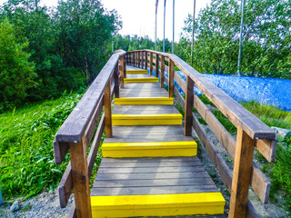 Obraz premium Wooden staircase with handrails and yellow steps, built for hiking in the forest strip.