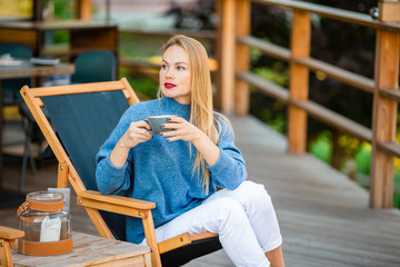 Fall concept - beautiful woman drinking coffee in autumn park under fall foliage