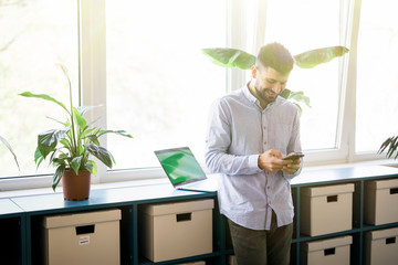 Technology makes it all easier. Smiling young man holding mobile phone and typing message while...