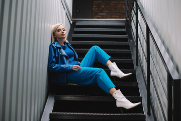 blonde woman wearing blue leather jacket and heels sitting on stairs