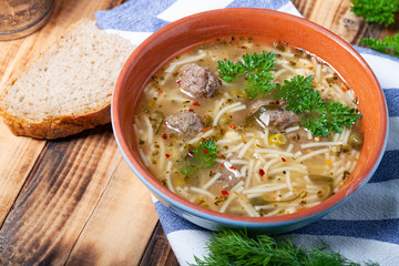 Homemade soup with noodles and meatballs on a wooden table. Traditional rural dinner