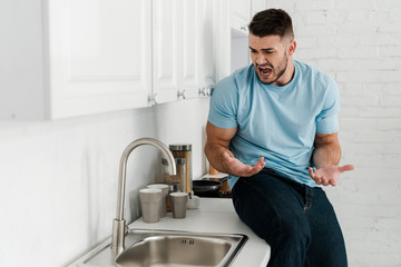 upset man gesturing and screaming near faucet in kitchen