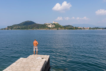 Lone fisherman on the shore of Lake Maggiore in Arona, Novara, Italy, on a sunny day