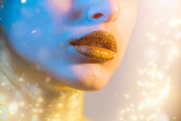 Gold Paint smudges drips from woman face, lips and hand, lipgloss   dripping from sexy lips, golden liquid drops on beautiful model girl's   mouth, gold metallic skin make-up. Beauty woman makeup clos