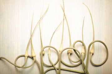Ripe garlic arrows on a light wooden background. Toned