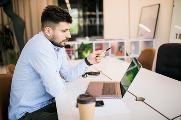 Young businessman working in office, sitting at desk, looking at laptop and pointed with pen on screen