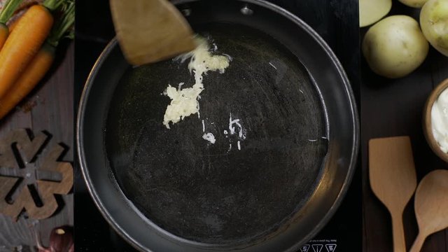 Flat lay video: chef stirs crushed garlic by wooden kitchen spatula on the hot pan, tabletop of cooking vegetarian food, fried garlic, blanch vegetables, Full HD Prore 422 HQ