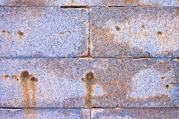 Aged colorful stone blocks, silver gray wall with rusty stains.