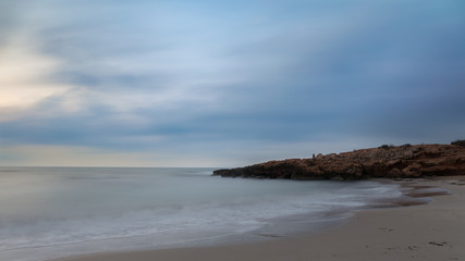 Fototapeta na wymiar Half an hour before sunrise. A beautiful bay for swimming with a sandy beach in the early morning before sunrise near the Spanish town of Torrevieja. Soft waves through long exposure.