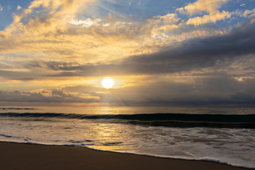 Fototapeta na wymiar A fantastic dreamlike sunrise over the Mediterranean on the Costa Blanca. A wave hits the sand beach with beautiful orange clouds in the sky.