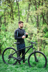 Fototapeta na wymiar Young man in track-suit with bicycle drinking water at summer park