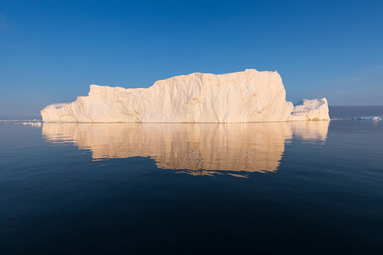 Photogenic and intricate iceberg under an interesting and blue sky during sunset. Effect of global warming in nature. Conceptual image of melting glacier in deep blue water in Antarctica or Greenland