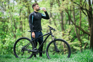 Fototapeta na wymiar Tired biker resting and drinking from water bottle in green park