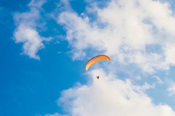 An orange paraglide flying on a cloudy sky