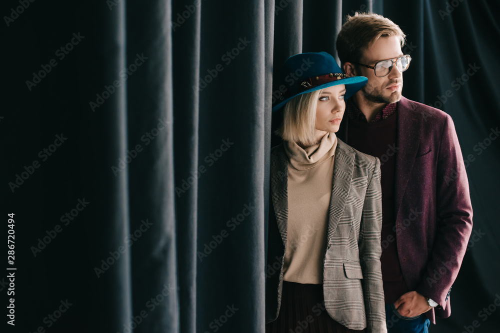 Wall mural stylish young woman and man standing with hand in pocket near curtain