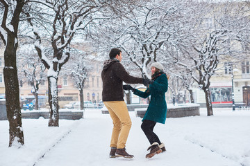 Fototapeta na wymiar Young loving couple dressed in plaid scarves walk, run and laugh at the old city in winter. man and woman in casual style are in the snow park