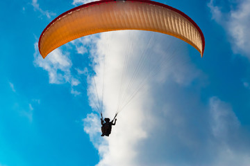 Orange paraglide flying on a cloudy sky