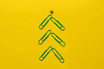 business year end concept: green paper clips in shape of Christmas tree and a pin as a star above on a yellow background