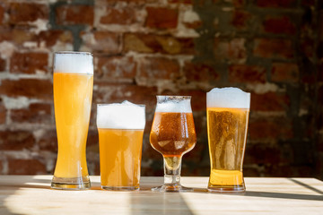 Glasses of different kinds of light beer in sunlight on brick wall background. Cold delicious alcohol drinks are prepared for a big friend's party. Concept of holiday, fun, meeting, oktoberfest.