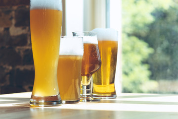 Glasses of different kinds of light beer in sunlight on brick wall background. Cold delicious alcohol drinks are prepared for a big friend's party. Concept of holiday, fun, meeting, oktoberfest.