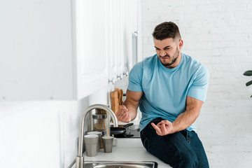 Fototapeta premium selective focus of emotional man showing middle fingers and looking at faucet in kitchen